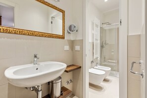 A modern bathroom with a large white sink, a gold-framed mirror, and a glass-enclosed shower area. - Oriana Homèl Udine (Udine)