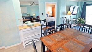 A dining area with a wooden table and chairs, a kitchen in the background, and a TV mounted on the wall. - Oceanfront 3BR/2B  Springs Towers 704  Pool, Hot Tub, Fitness Room (North Myrtle Beach)