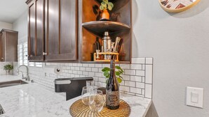 Cocina con alacenas de madera oscura, salpicadero de azulejos blancos, encimera de mármol y una botella de vino como adorno central.