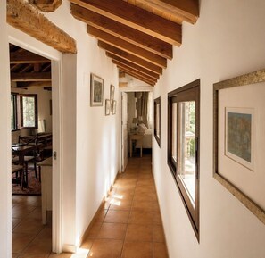 A corridor with wooden beams, framed pictures on the walls, and a dining area with tables and chairs on the left.