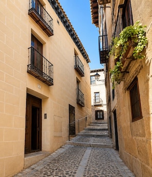 A narrow cobblestone street flanked by buildings with balconies and a clear blue sky.