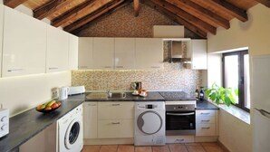 A kitchen with wooden beams, white cabinets, a washing machine, an oven, and a window with plants. - Céntrico impresionante ático con vistas del cathedral  (Toledo)