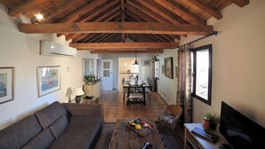 A spacious living room with a high wooden ceiling, a sofa, a dining table with chairs, and a television. - Céntrico impresionante ático con vistas del cathedral  (Toledo)