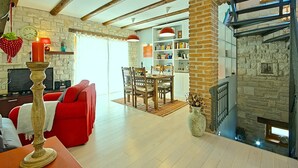 A cozy living room with a red sofa, a wooden dining table, and a fireplace. - Sea view, garden with barbecue, pool with loungers, parking, air conditioning, wifi (Rojci)