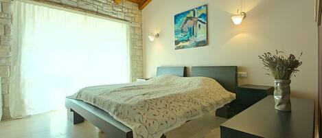 A bedroom with a bed, a stone wall, a painting, and a vase with flowers.