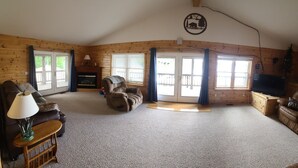Ein gemütlicher Wohnraum im Chalet-Stil mit Kamin, zwei Sofas, einem Fernseher und einer Holzbalkendecke.