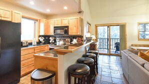 A spacious kitchen with wooden cabinets, a large island with stools, a refrigerator, and a microwave.