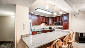 Una cocina con encimeras de granito, armarios de madera, una isla central con taburetes de bar, iluminaci ón colgante y un microondas.