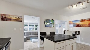 A modern kitchen with a central island, a dining area with chairs, and a living space with a sofa and a coffee table. - Ocean Breeze Villa 🏝️ 5 Minute Walk to Beach (Pompano Beach)