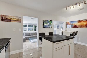A modern kitchen with a central island, a dining area with chairs, and a living space with a sofa and a coffee table. - Ocean Breeze Villa 🏝️ 5 Minute Walk to Beach (Pompano Beach)