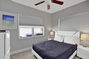 Ein Schlafzimmer mit einem Bett, zwei Nachttischen mit Lampen, einem Deckenventilator und einem Fenster mit Jalousien.
