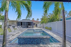 A swimming pool with lounge chairs and a patio area, surrounded by palm trees and a white fence. - Ocean Breeze Villa 🏝️ 5 Minute Walk to Beach (Pompano Beach)