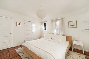 A bedroom with a large bed, white walls, and a ceiling light fixture. - Venice Beach Cottage with incredible outdoor space! (Venice)