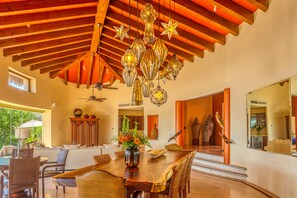 A spacious dining area with a large wooden table, wicker chairs, and a chandelier.