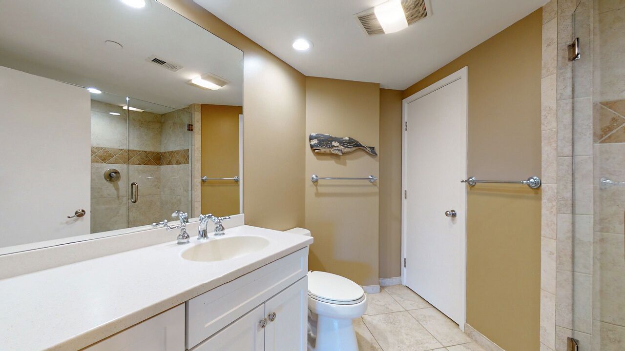 A bathroom with a white sink, mirror, and toilet, a glass shower enclosure, and beige walls.