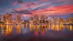 A waterfront cityscape with high-rise buildings, a marina with boats, and a sunset sky.