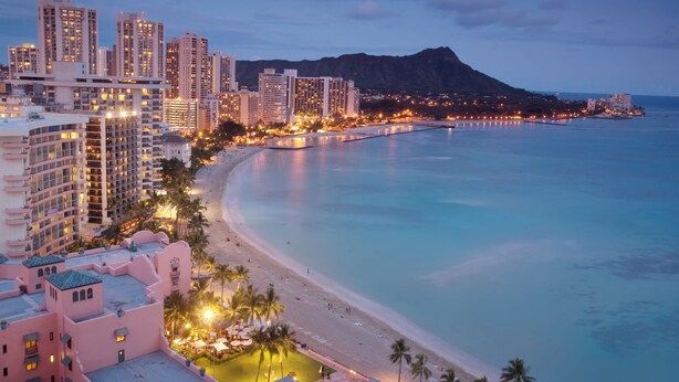 A coastal cityscape with high-rise buildings, a beach, and a mountain in the background.