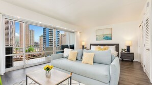 A modern living room with a large sofa, a coffee table, and a view of tall buildings through floor-to-ceiling windows.