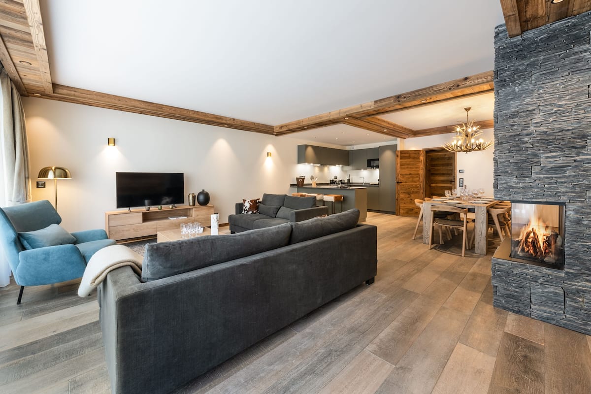 Ein modernes Wohnzimmer mit einem großen, grauen Ecksofa, einem Flachbildfernseher und einem Kamin aus Naturstein.