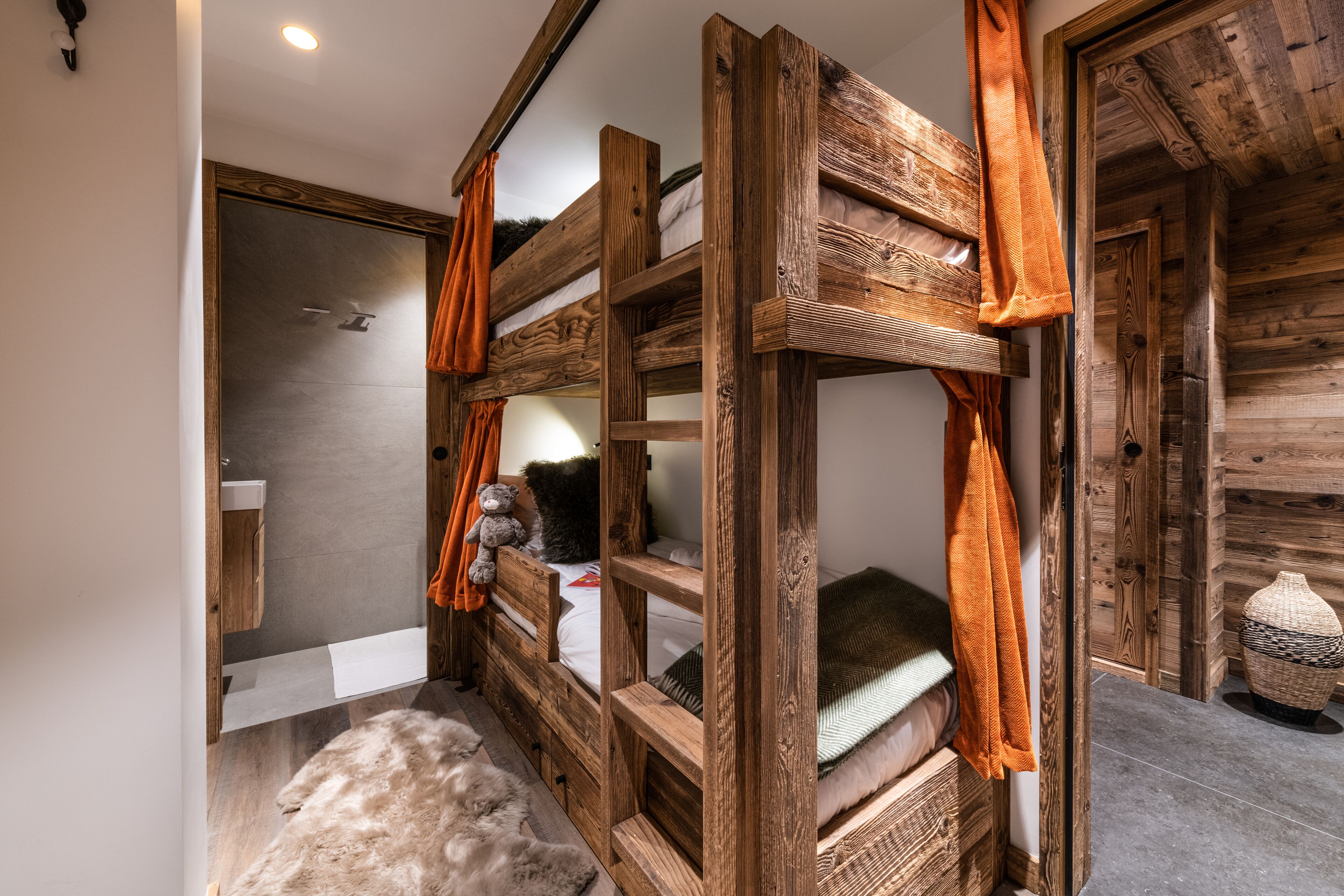 Una cama litera de madera, un estante pequeño con un osito de peluche y una cesta tejida en el suelo.