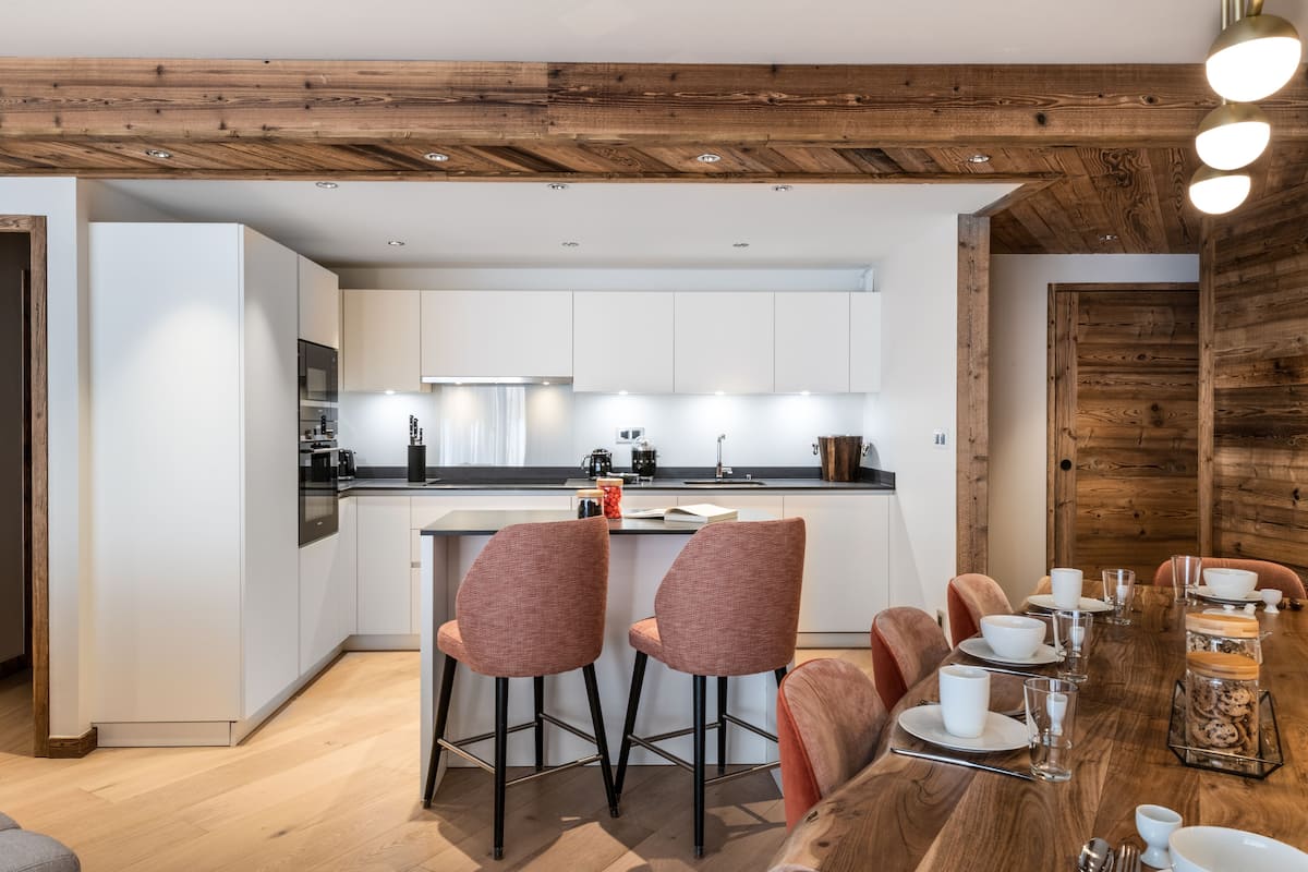 Eine moderne Küche mit weißen Schränken, einer zentralen Kochinsel und einem Essbereich mit Holztisch und Stühlen.