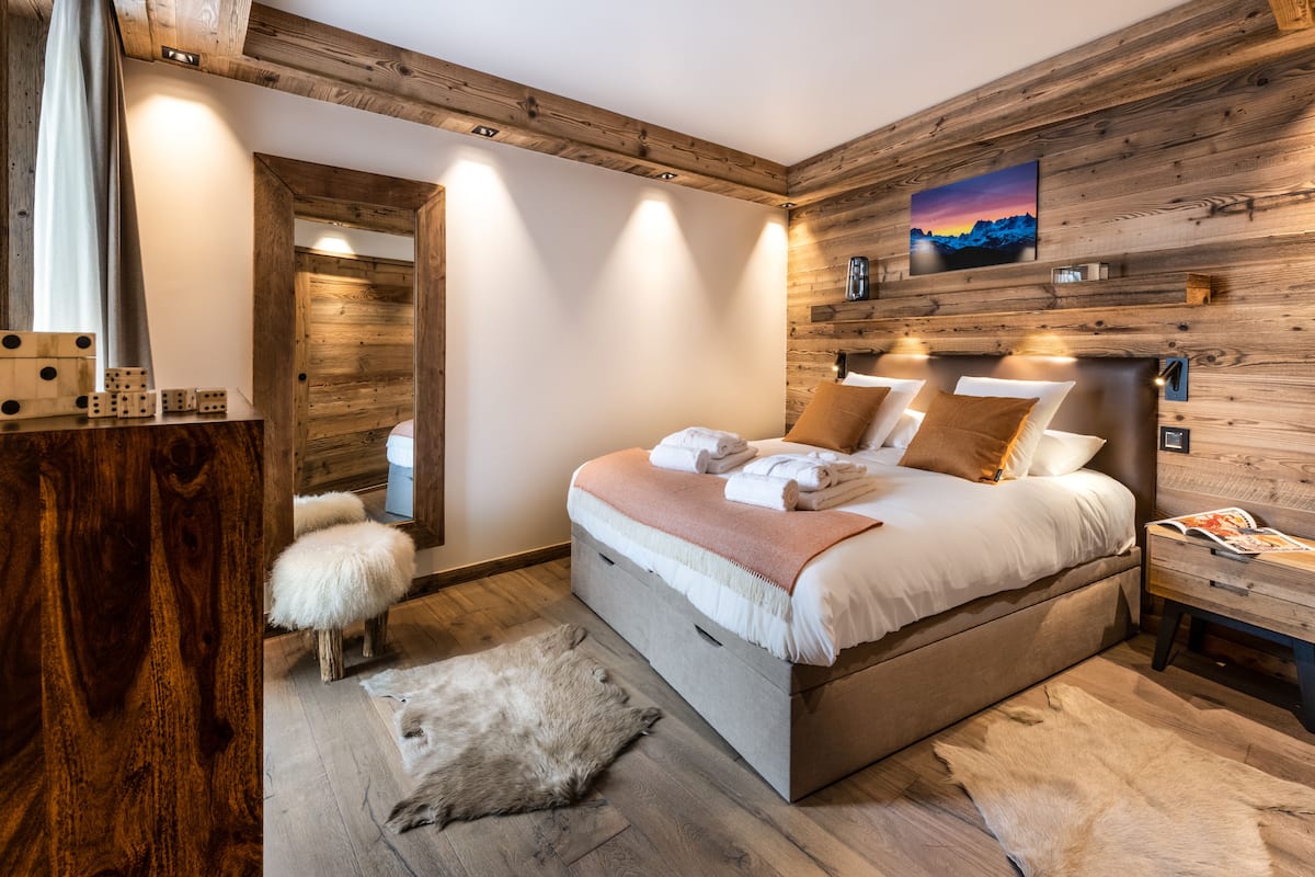 Ein Schlafzimmer mit Holzwandverkleidung, einem Bett mit Kissen, einem Nachttisch und einem Fellteppich.