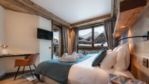 Une chambre d’hôtel moderne avec un plafond en bois, un grand lit avec une literie blanche, un bureau avec une chaise et un téléviseur fixé au mur.