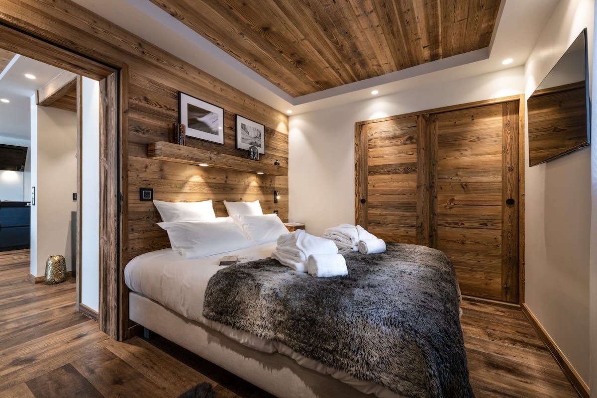 Ein Schlafzimmer mit einem Holzkopfteil, einem großen Bett mit weißer Bettwäsche, einem Fellüberwurf und einem Holzschrank.