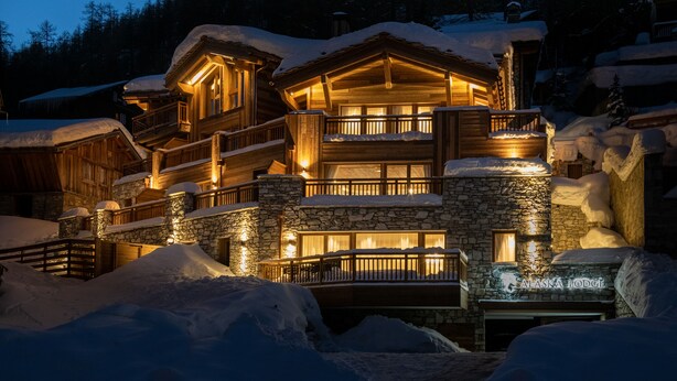 Un chalet à étages, construit en pierre et en bois, doté de balcons et de grandes fenêtres.