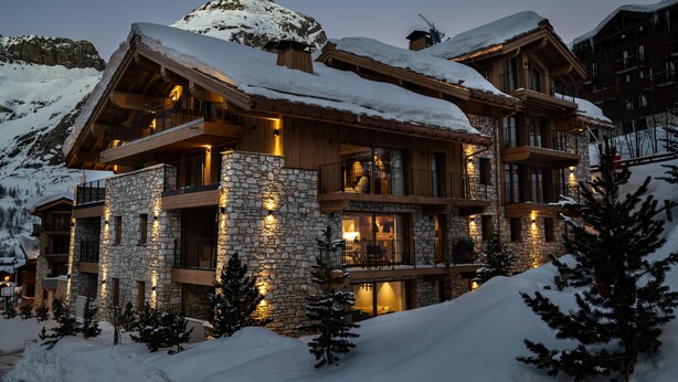 Un lodge a più piani con pareti in pietra e balconi in legno, circondato da montagne innevate.