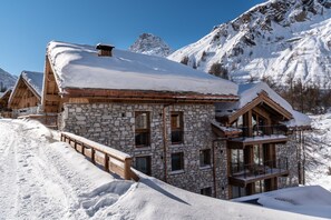 A stone building with a wooden balcony, surrounded by snow-covered mountains. - Vail Lodge by Alpine Resorts (Val-d'Isere)