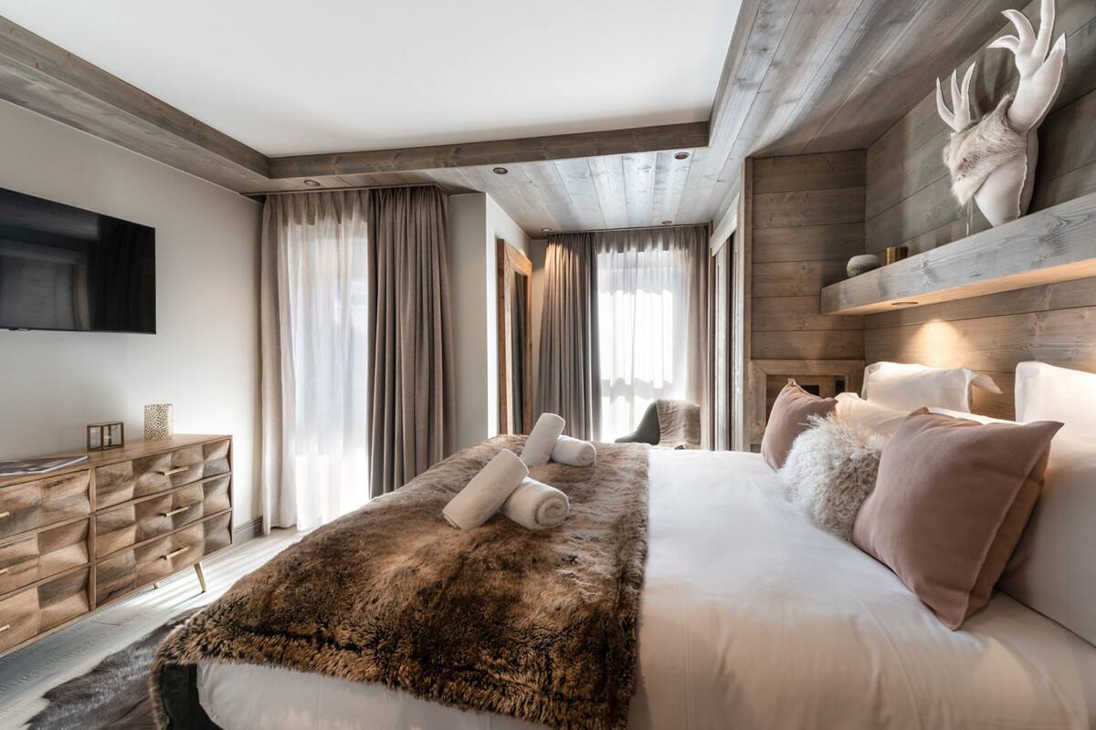 A modern bedroom with a large bed, a wooden dresser, and a mounted TV.