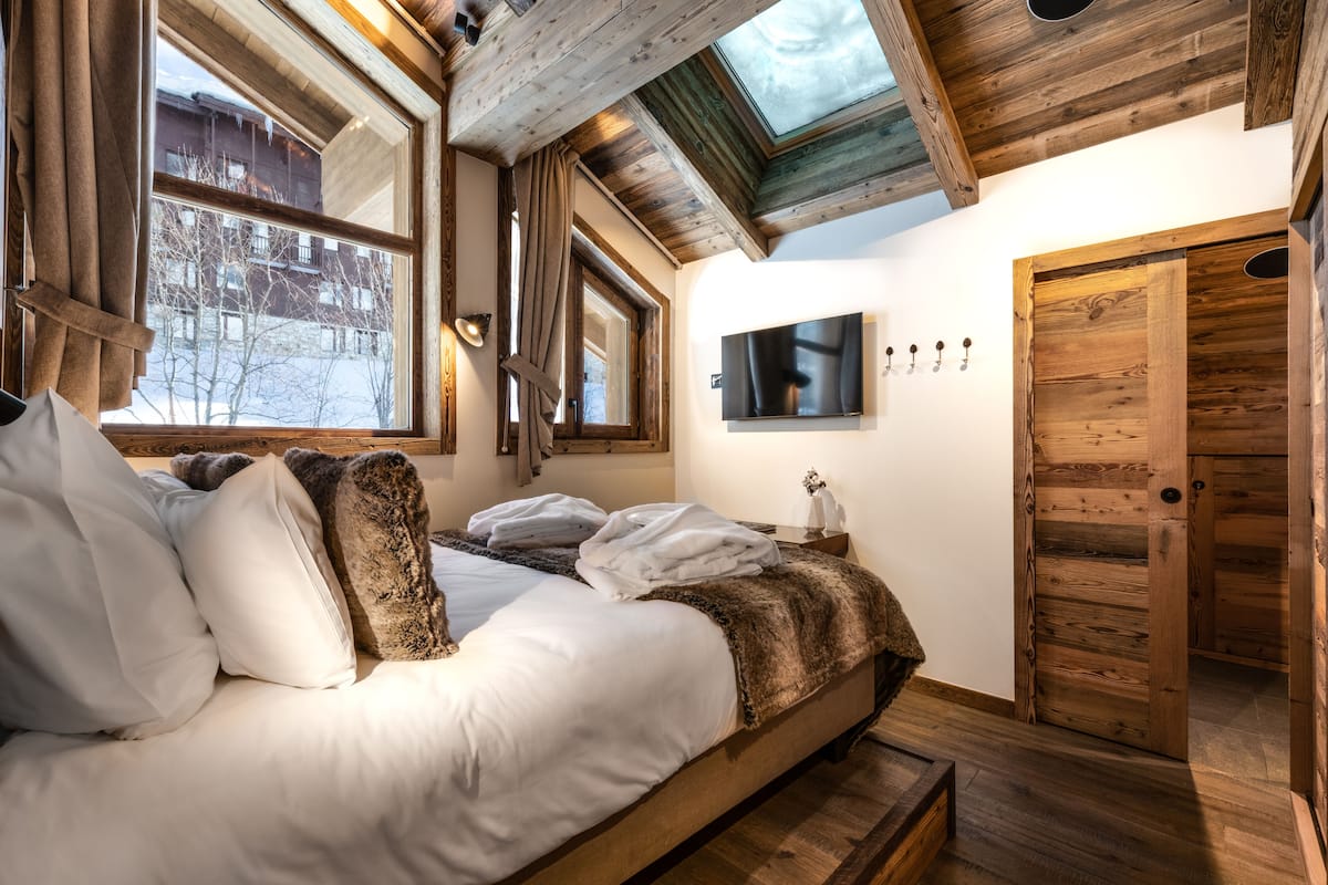 A wooden bedroom with a bed, a skylight, a TV, and a wooden door.
