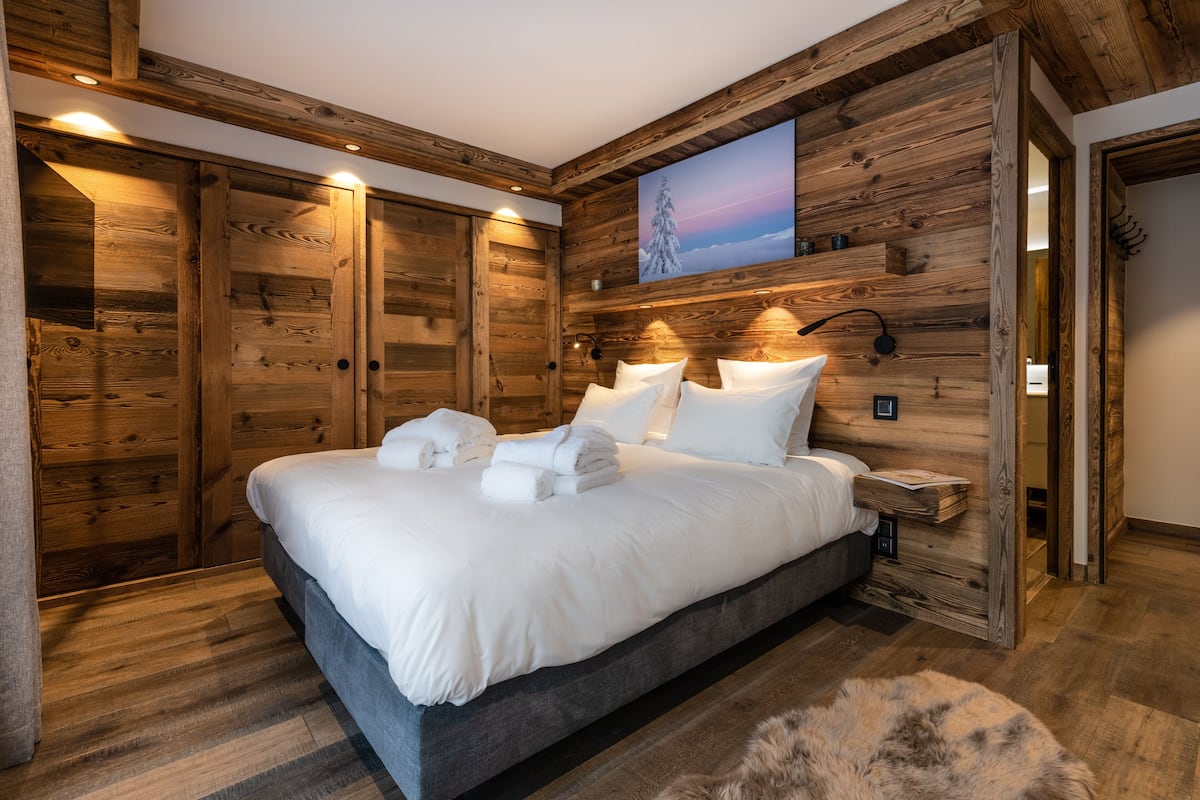 A bedroom with a large bed, wooden walls, and a painting of a snowy mountain.