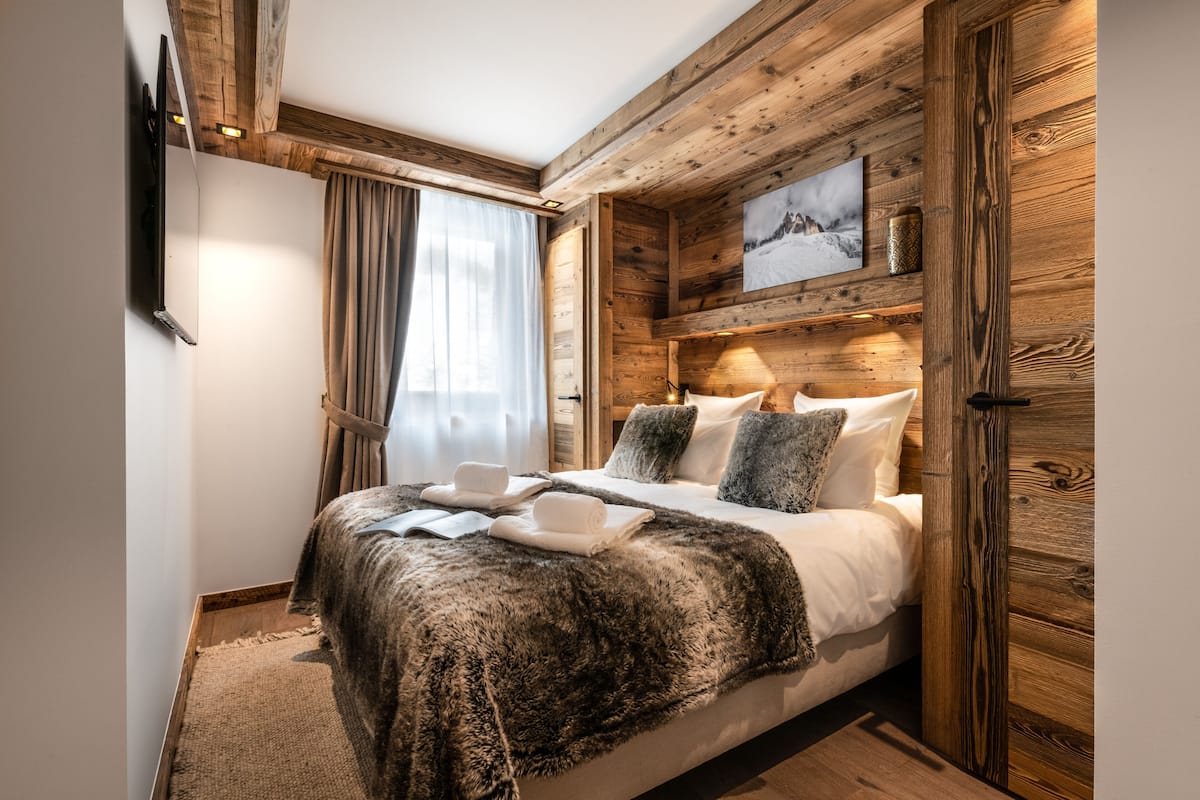 A wooden-paneled bedroom with a bed, a flat-screen TV, and a painting on the wall.