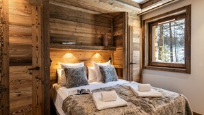 Camera da letto in stile baita in legno con un letto grande, due cuscini, una coperta in pelliccia e una finestra vista alberi.