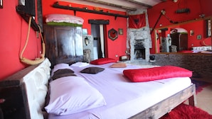 Una cama con almohadas y una manta roja, una chimenea de piedra y una pared roja.