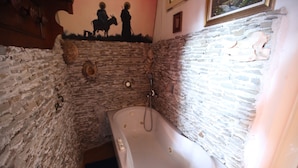 Un baño con pared de piedra, una bañera y decoración rústica que incluye la silueta de una vaca y un armario de madera.