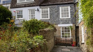 A narrow alleyway leading to a stone house with a wooden gate, surrounded by lush greenery and adjacent residential buildings. - Stone cottage in central Salcombe sleeps 8  (Salcombe)