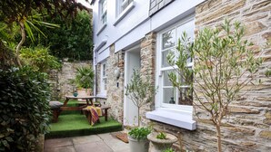 A stone building with a small garden area featuring a table, chairs, and potted plants. - Stone cottage in central Salcombe sleeps 8  (Salcombe)