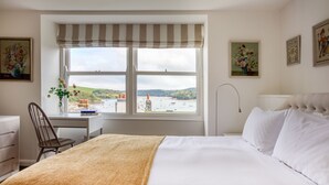 A hotel room with a large bed, a desk with a chair, a window with a view of a landscape, and artwork on the walls. - Stone cottage in central Salcombe sleeps 8  (Salcombe)