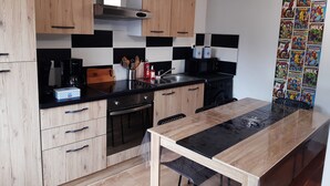 A modern kitchen with wooden cabinets, a black countertop, and a dining area. - "Les 4 Fils Aymon" House overlooking the Meuse. (Bogny-sur-Meuse)