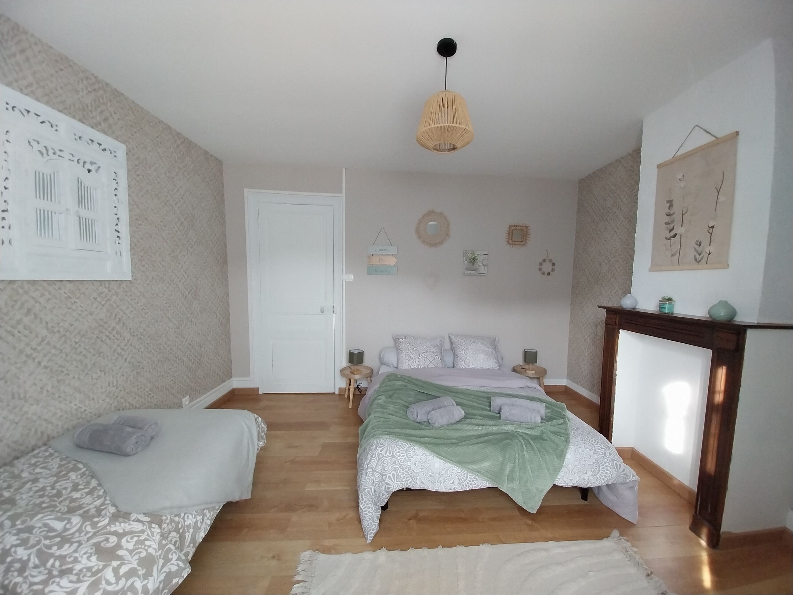 A bedroom with a bed, two bedside tables, a hanging light fixture, and a fireplace.