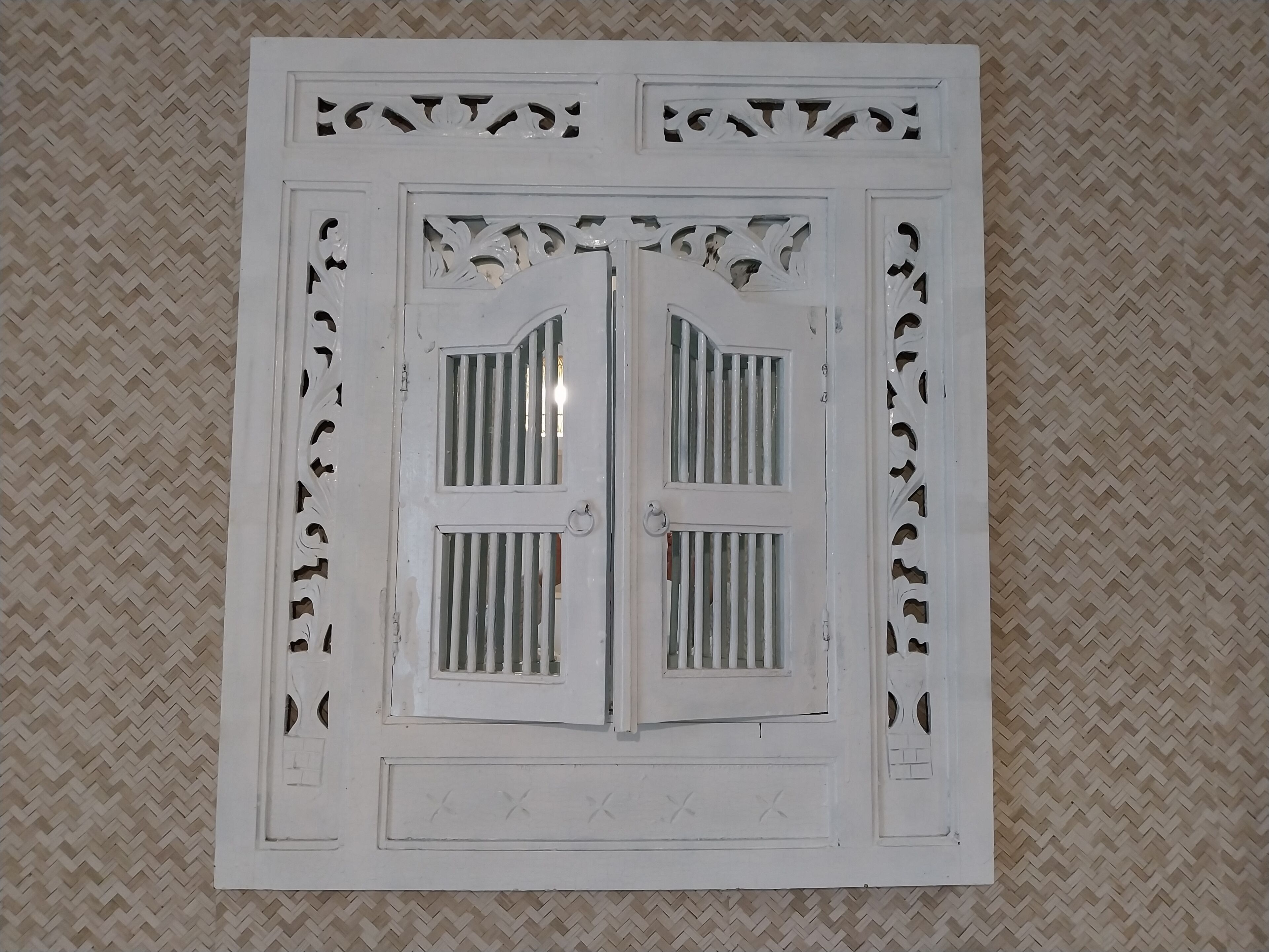 Un panneau décoratif blanc orné de motifs complexes découpés et doté d’une porte centrale avec des fenêtres grillagées.