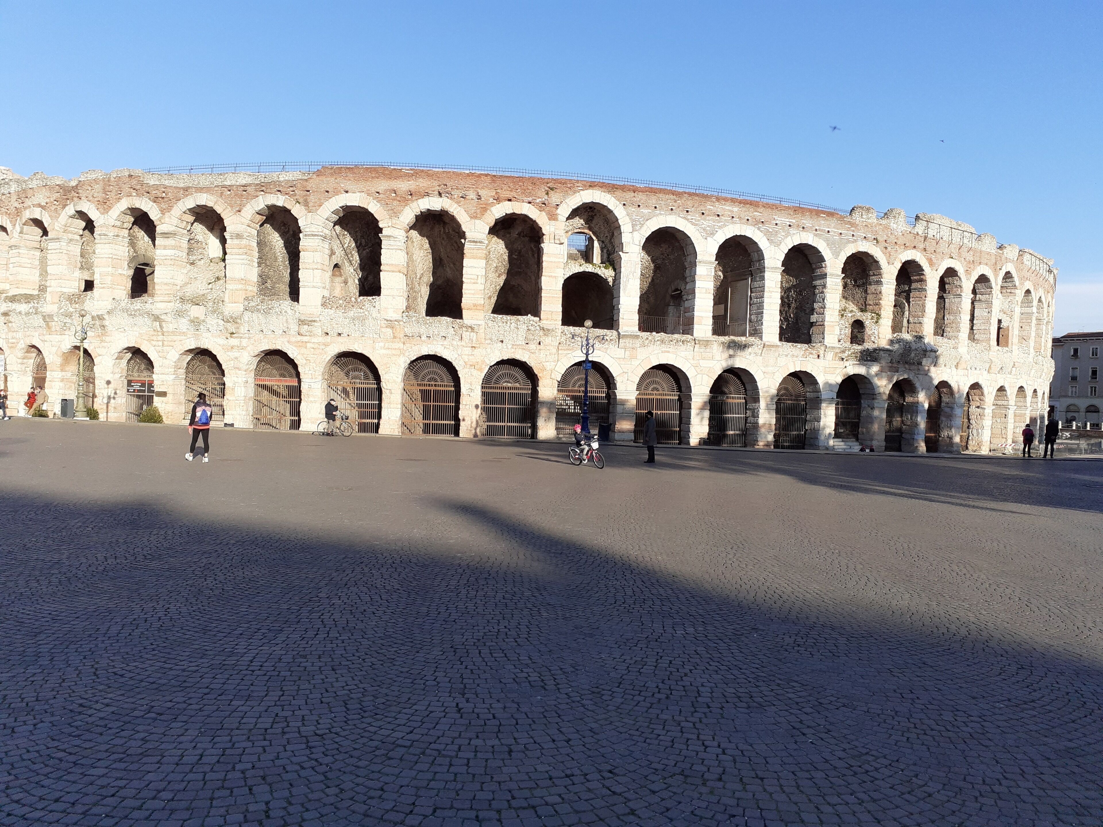 Un grande edificio storico in pietra con numerose arcate e una piazza lastricata.