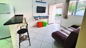 Een compact woongedeelte met een kitchenette, een aan de muur bevestigde televisie, een bank en een eethoek met een stoel.