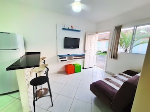 Um espaço de estar compacto com cozinha compacta, televisão na parede, sofá e área de jantar com uma cadeira.