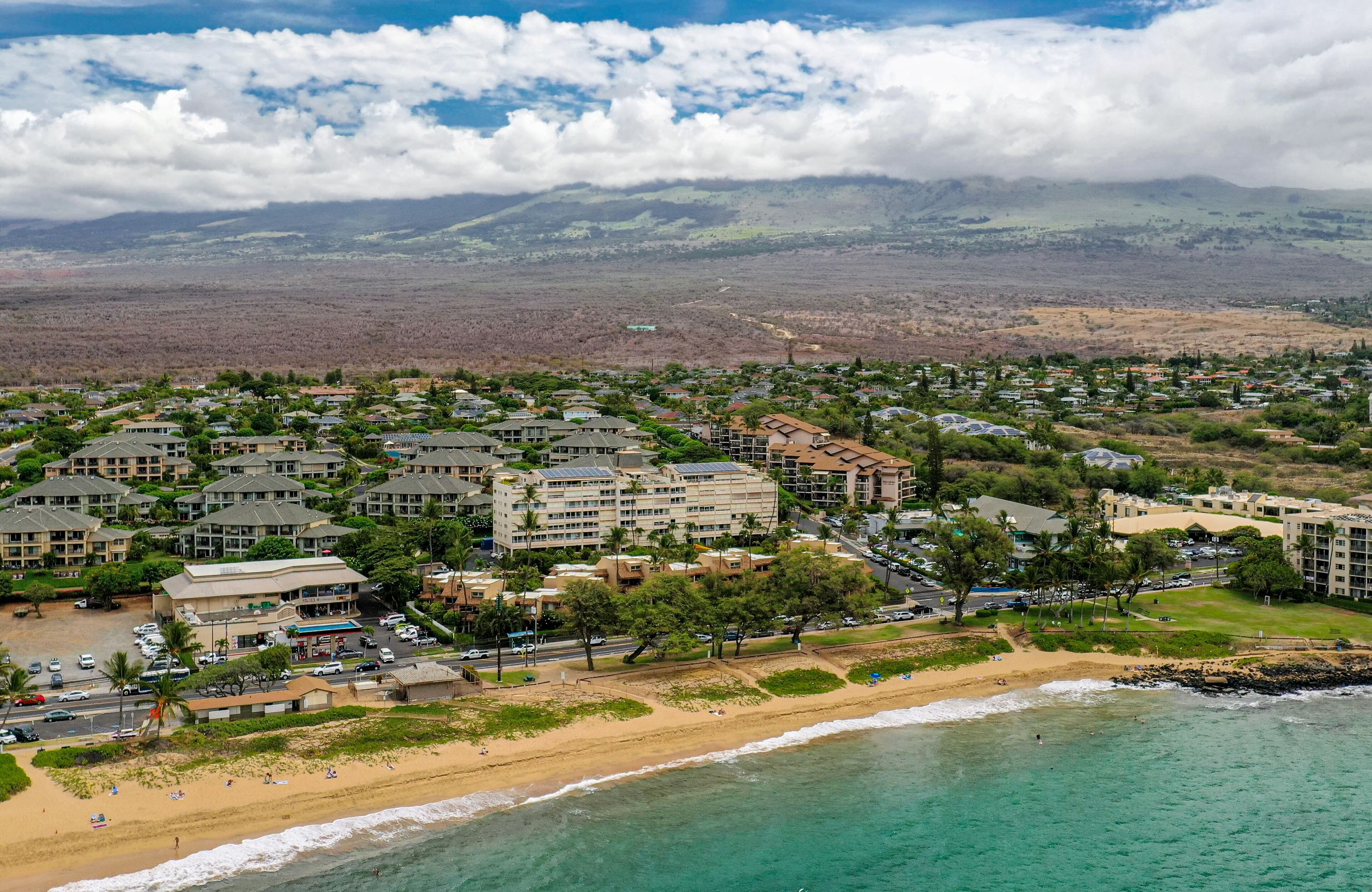 A coastal resort with multiple buildings, a beach, and a mountainous backdrop.