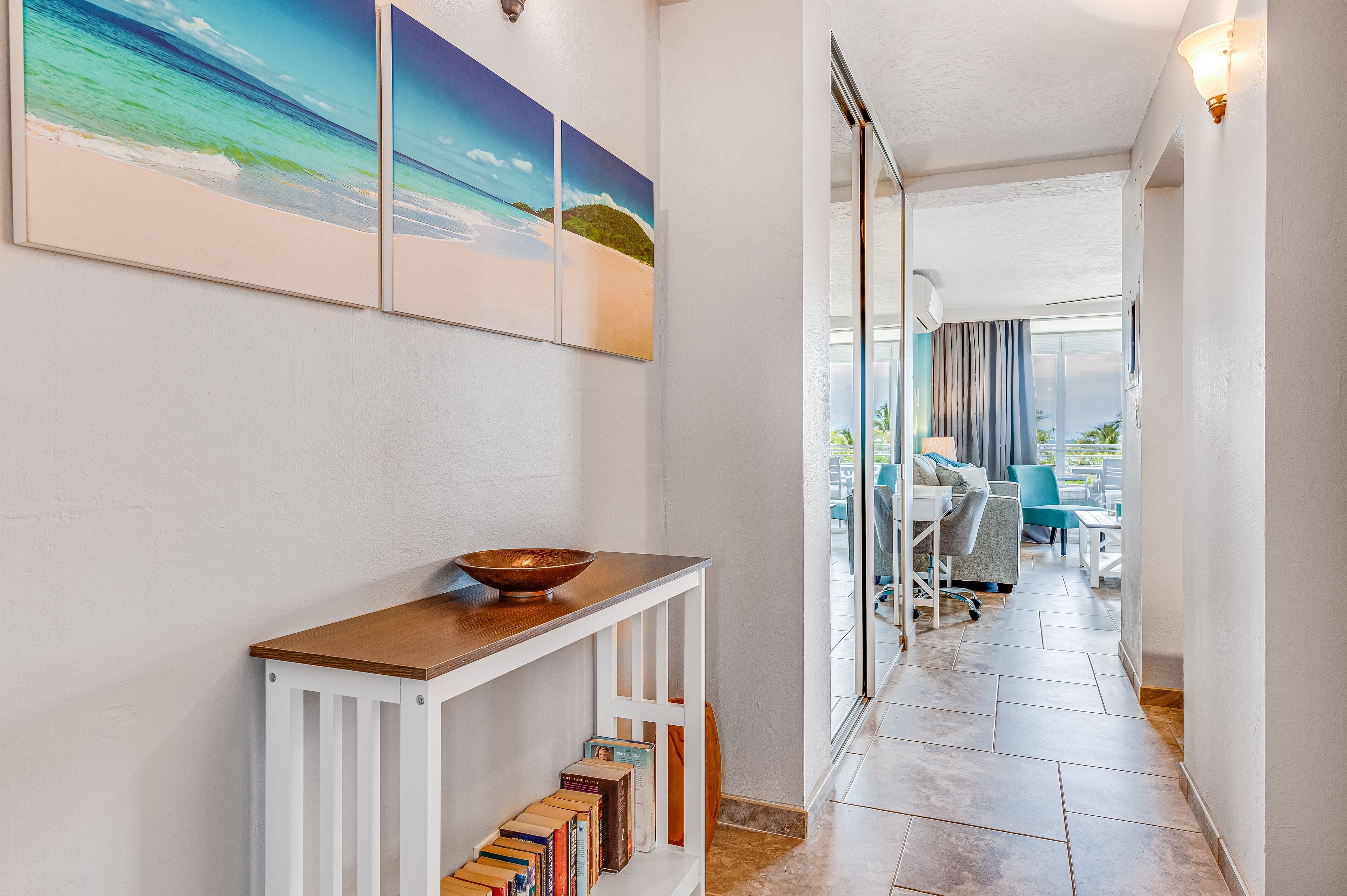 A hallway with a wooden console table, books, and a view to a balcony area with outdoor seating.