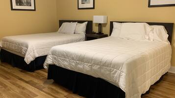 Two single beds with white bedding, a nightstand with a lamp, and framed pictures on the wall.